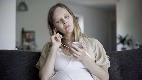 Front-view-of-happy-pregnant-woman-choosing,-listening-to-music